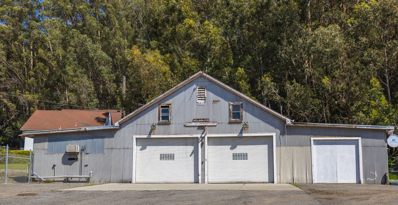 A rustic metal garage with a corrugated facade surrounded by dense trees.
