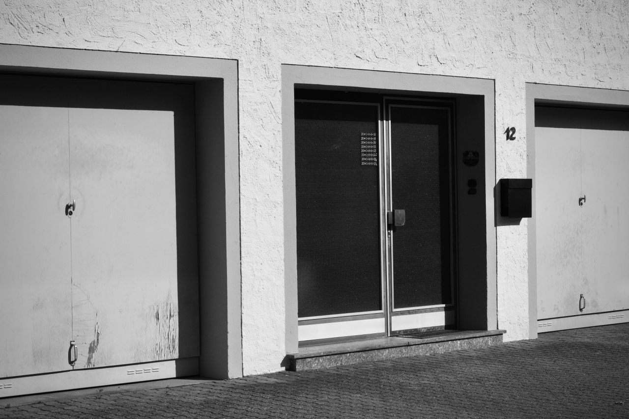 heros-img Monochrome photo of an urban building facade with garages and doors.