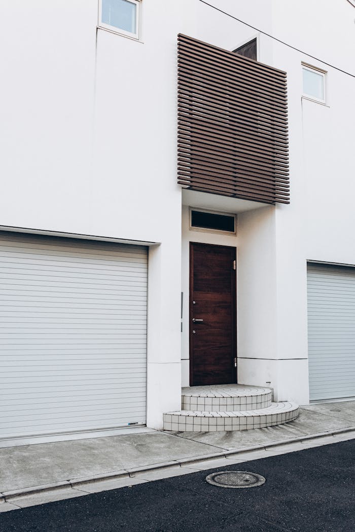 services-02 Contemporary white building facade with wooden door and twin garage entrances.