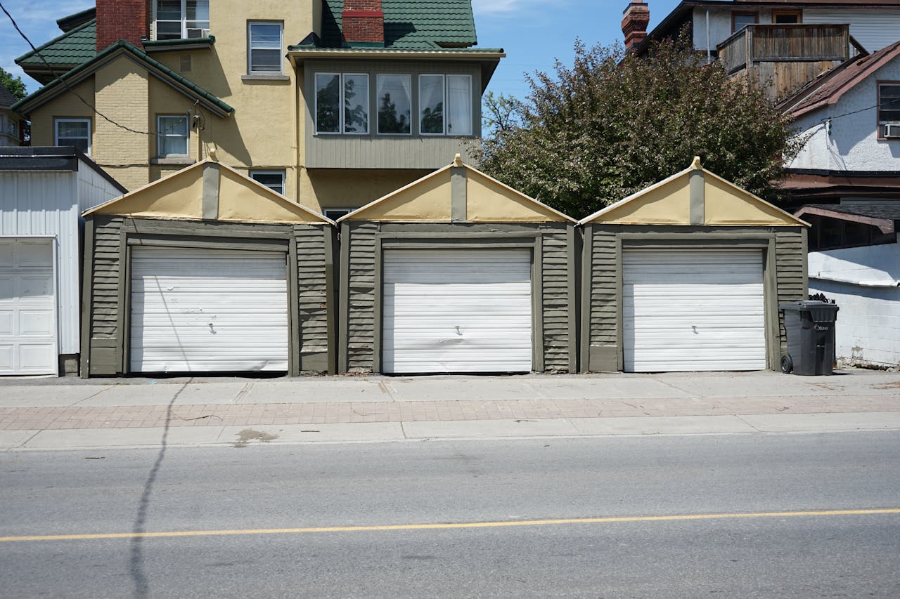 about-us-02 Row of three traditional residential garages with unique roof design on a sunny day.